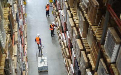 Above view of warehouse workers moving goods and counting stock in aisle between rows of tall shelves full of packed boxes